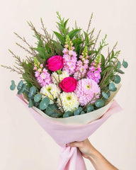 Colourful bouquet with snapdragons, roses & greenery. Wrapped in pink tissue paper.