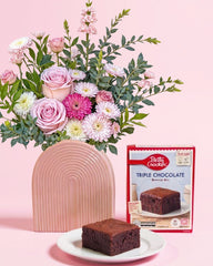 Floral arrangement with a pink vase, a slice of brownie, and Betty Crocker brownie mix packaging on a pink background.