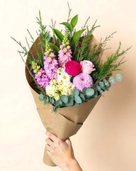 Bouquet of flowers wrapped in brown paper held by a hand against a beige background