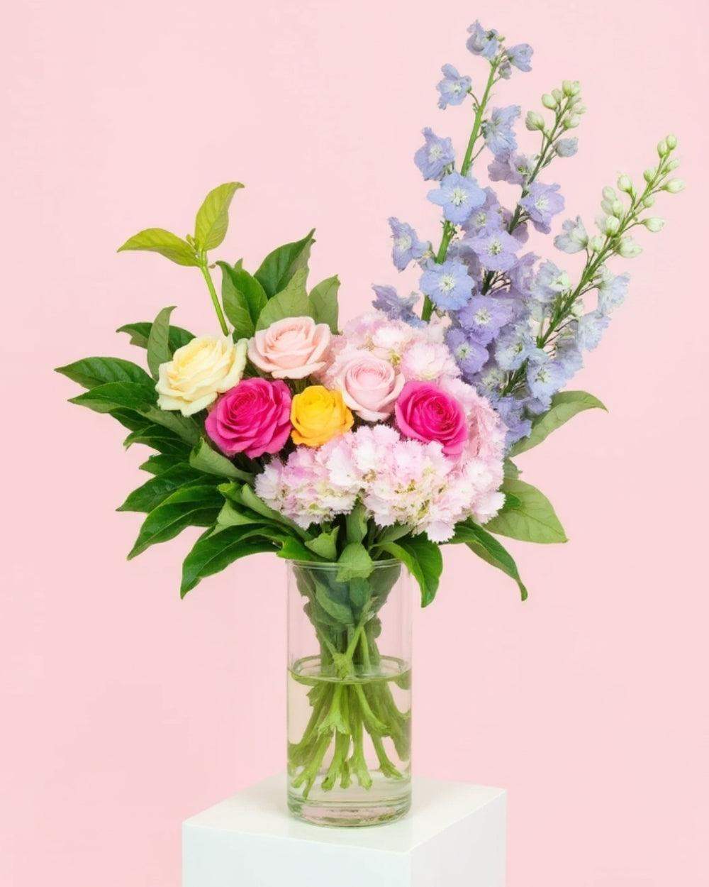 Pastel Bouquet of flowers in a glass vase standing on a white pedestal.