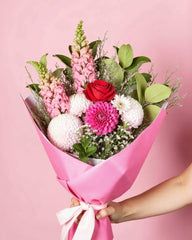 I Love You Bouquet featuring an assortment of pink and red flowers with greenery. The flower bouquet is wrapped in dark pink tissue paper and includes aa light pink ribbon.
