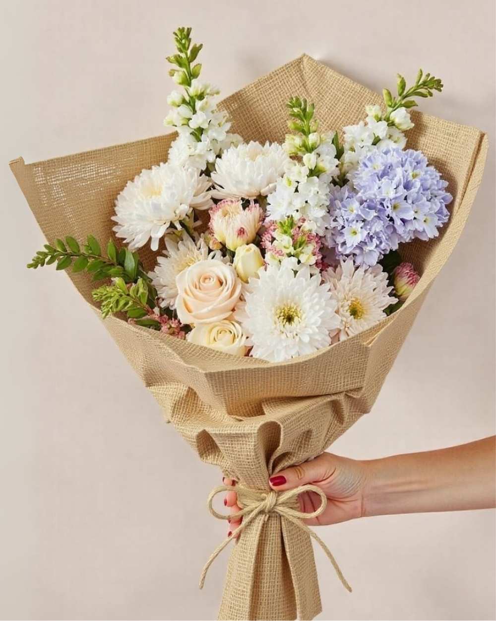 Bouquet of flowers wrapped in brown paper held by a hand on a beige background