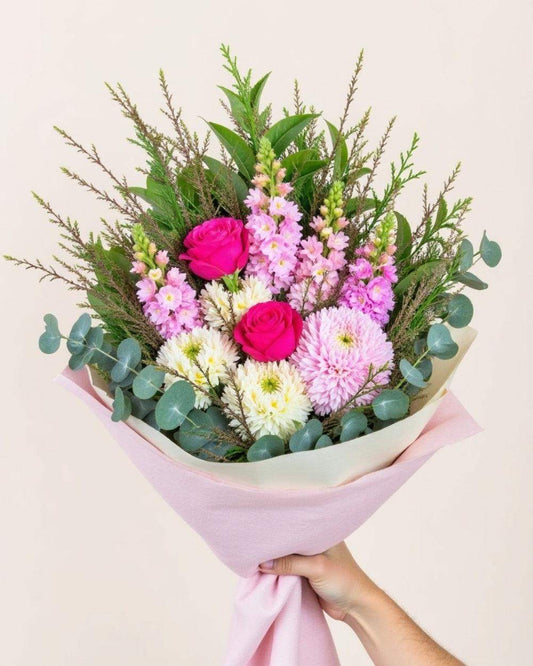 Colourful bouquet with snapdragons, roses & greenery. Wrapped in pink tissue paper.