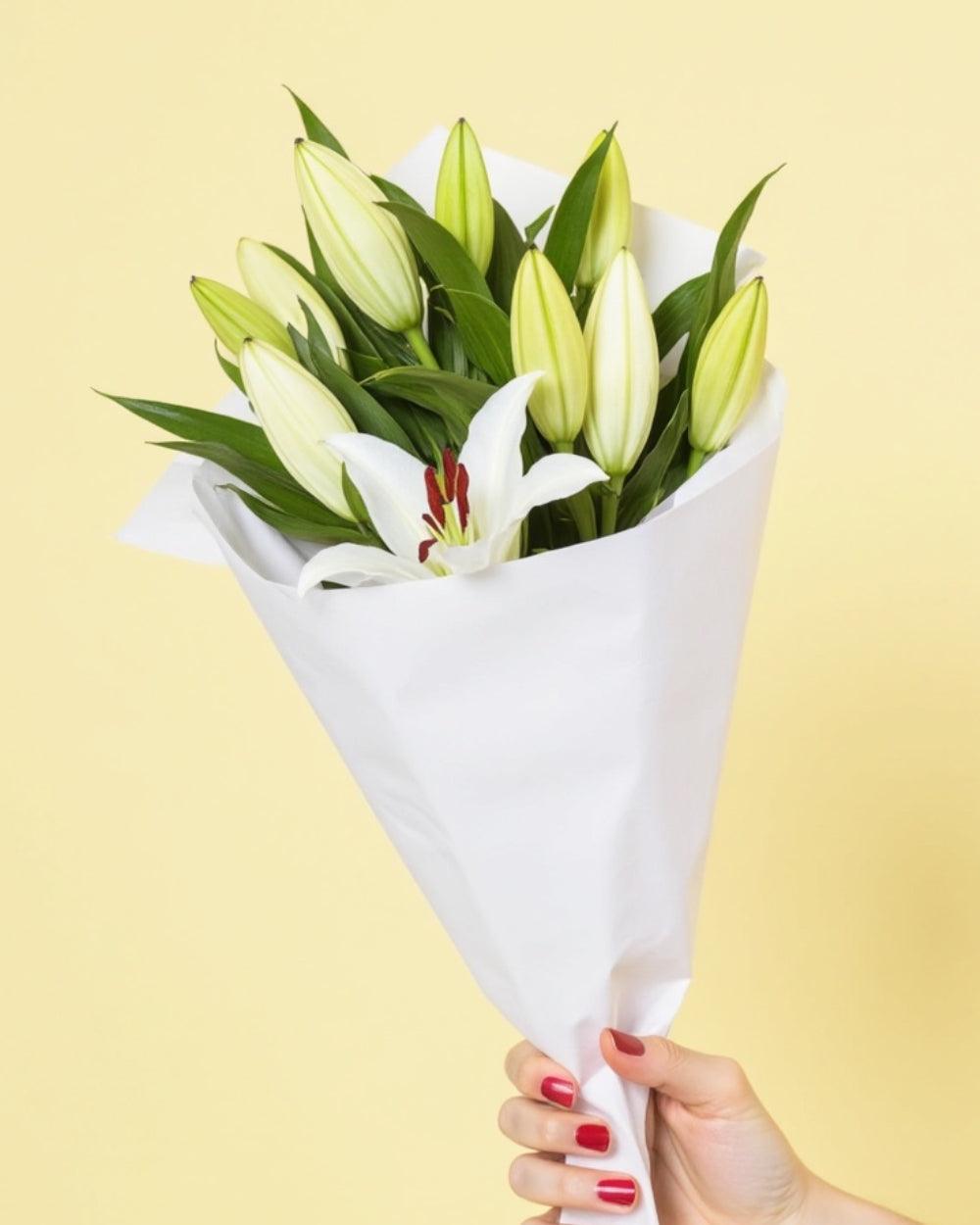 Lilies Bouquet featuring 10 unopened lily buds. The bouquet is handheld and wrapped in white tissue paper.