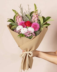 Bouquet of flowers wrapped in brown paper held by a person against a beige background